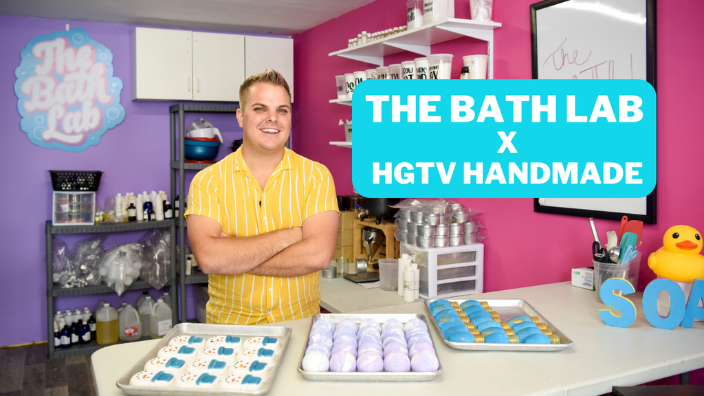 Man in yellow striped shirt with arms crossed smiling at the camera for a photo shoot with HGTV. Trays of bath bombs are on the table along with a rubber duck.